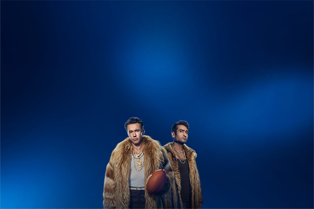 Two men in fur coats promoting sports streaming.