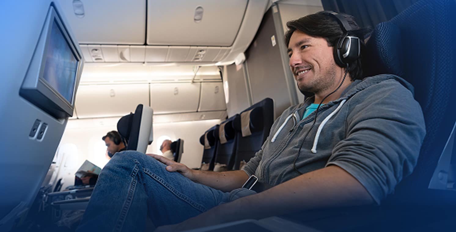 DIRECTV FOR BUSINESS. Man watching TV with headphones on a plane.